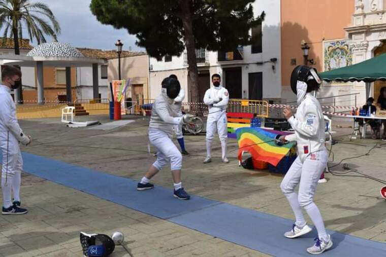 Dos competidors d'esgrima lluitant amb banderes de fons de LGBT| La robera sala d'armes