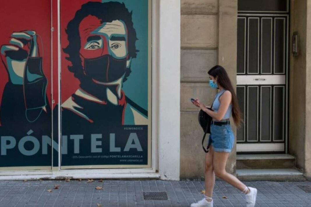 Xica caminant davant un cartell de Fernando Simón amb mascareta