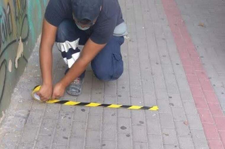 Una persona senyalitzant la distància de seguretat amb cinta groga i negra