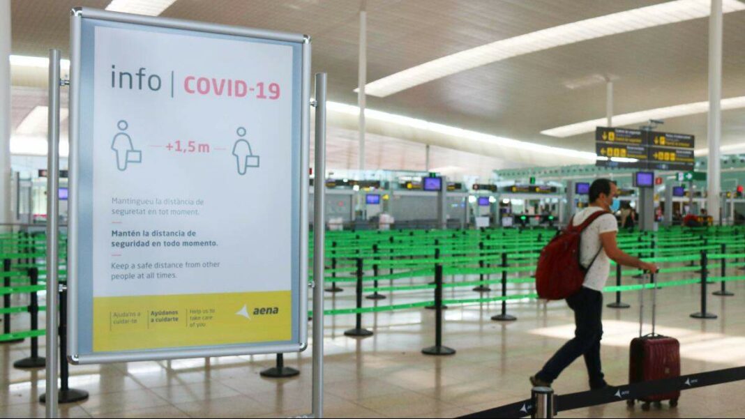Un cartell informatiu de la Covid-19 i un passatger a la T1 de l'Aeroport del Prat, pràcticament buit.