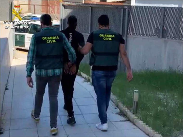 Dos guàrdies civils d'esquenes amb un detingut arrestat